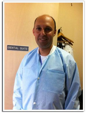 The image shows a man wearing a white lab coat standing in front of a sign that reads Dental Suite.