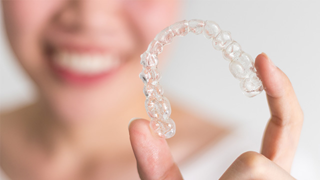 The image shows a person holding up a transparent dental retainer with their hand.